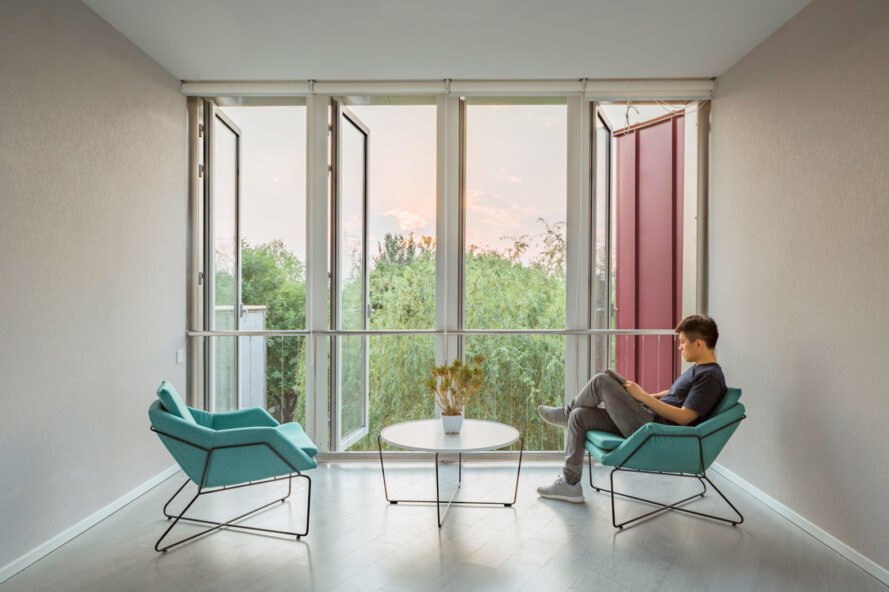 person sitting in teal chair beside open full-height windows