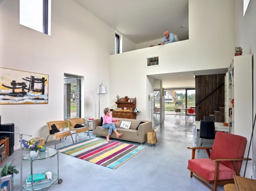 beige sofa, colorful striped rug and red chair in a double-height white living room