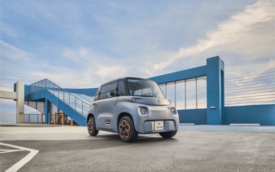 tiny gray electric car parked in front of a blue building